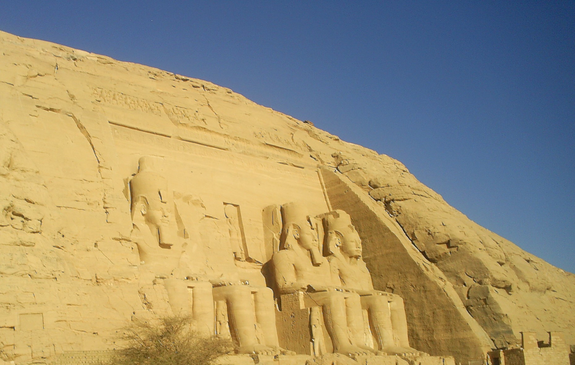 Exterior of the Temple of Abu Simbel, Egypt. A sandstone hill against a blue sky with enormous statues of seated pharaohs.