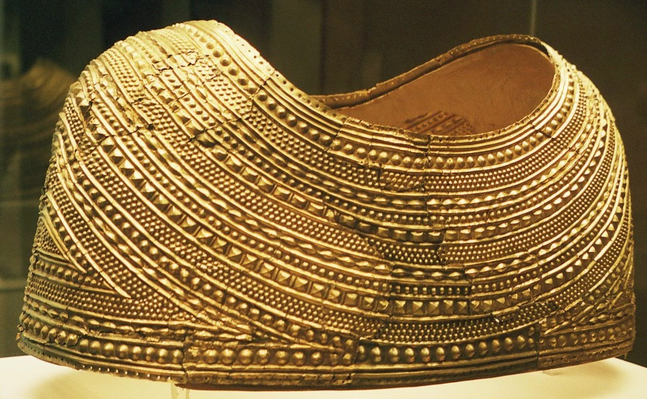 A golden mantle or cape in a museum display case. The mantle covers the shoulders and comes to about halfway down the upper arm.