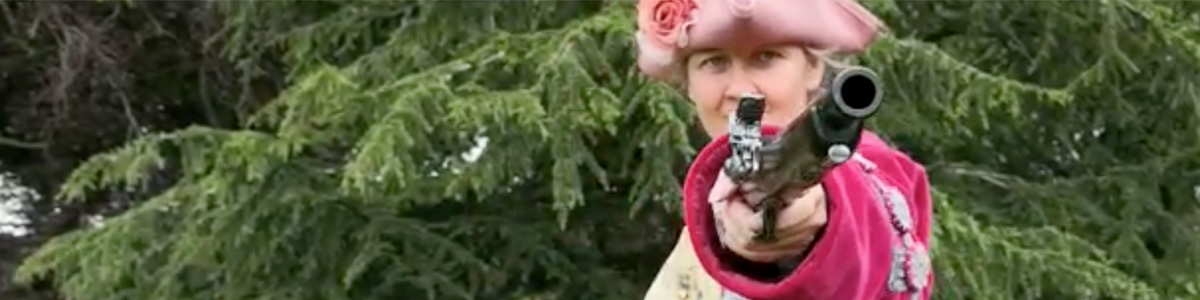 A Lady Pirate pointing a replica pistol into the camera against a background of trees