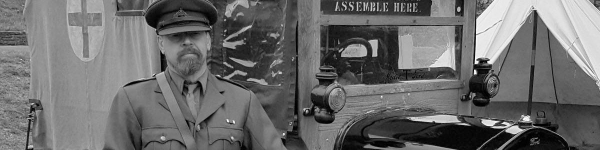 A black and white image of a marvellous history visitor dressed in WW1 costume standing in front of a WW1 vehicle